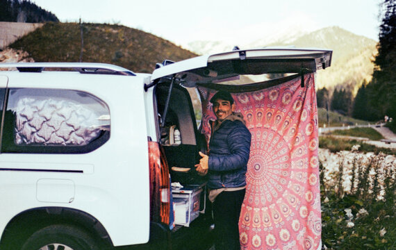 man making breakfast in minivan with open door covered by sarong