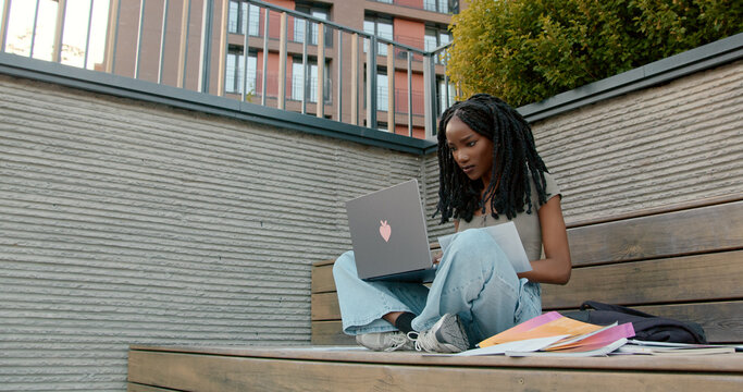 Focused university student studying with laptop and notes outdoors