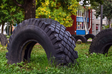 Old car tires buried in a lawn form a makeshift playground in a residential courtyard in Narva, Estonia. An urban autumn scene in soft evening light.