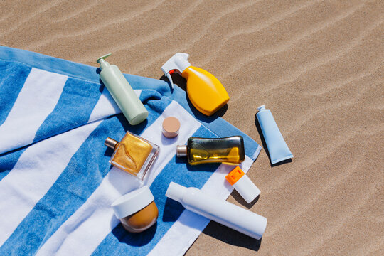 Sunscreen, tanning oil, moisturizer and perfume lying on beach towel