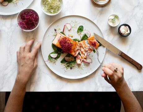 Woman eating grilled salmon with salad at marble table