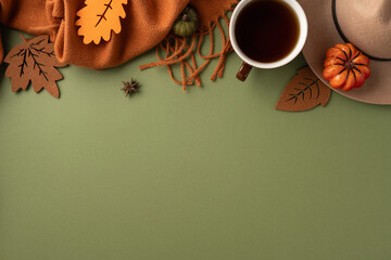 Stylish autumn arrangement featuring a warm scarf, tea, leaves, and pumpkin on green surface
