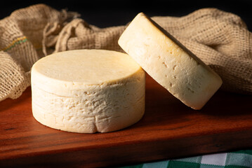 Semi-cured cheese made in Minas Gerais, Brazil, on a rustic surface and dark background, selective focus.