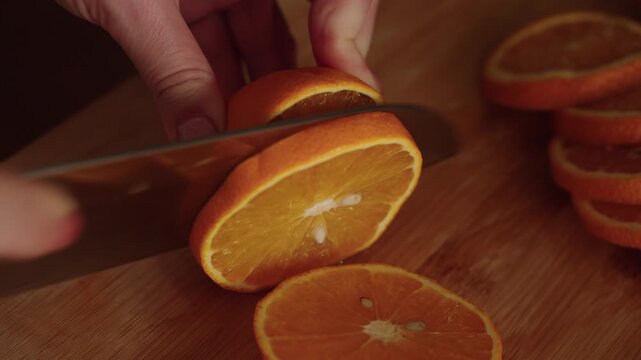 Vegan female cutting fresh, juicy orange into slices on wooden cutting board, preparing fresh ingredient for culinary creation at home, close-up. Concept of healthy lifestyle. Shooting in slow motion.
