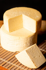 Semi-cured cheese made in Minas Gerais, Brazil, on a rustic surface and dark background, selective focus.