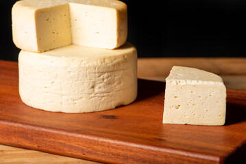 Semi-cured cheese made in Minas Gerais, Brazil, on a rustic surface and dark background, selective focus.