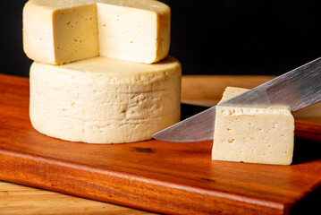 Semi-cured cheese made in Minas Gerais, Brazil, on a rustic surface and dark background, selective focus.