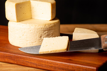 Semi-cured cheese made in Minas Gerais, Brazil, on a rustic surface and dark background, selective focus.