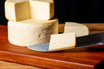 Semi-cured cheese made in Minas Gerais, Brazil, on a rustic surface and dark background, selective focus.