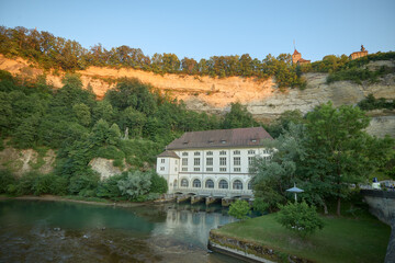 Fototapeta premium Serenity by the river with a historic building against limestone cliffs at sunset