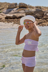 Young girl enjoying a sunny day at the beach wearing a stylish swimsuit and sun hat, smiling while playing in the water