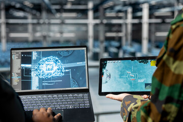 Close up of military operator and IT expert in army data center using AI on laptop to manage autonomous defense systems. Soldier and programmer using AI for strategic threat detection