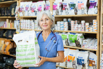 Smiling elderly veterinarian offering a package of healthy dry pet food. High quality photo