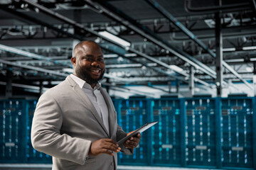 Happy technician in server hub checking recovery plan on tablet, monitoring energy consumption. Smiling data center employee using device, making sure sensors are functioning optimally