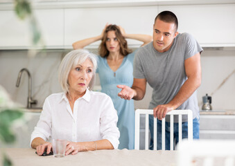 Couple of adult man and woman during family quarrel with elderly woman in kitchen