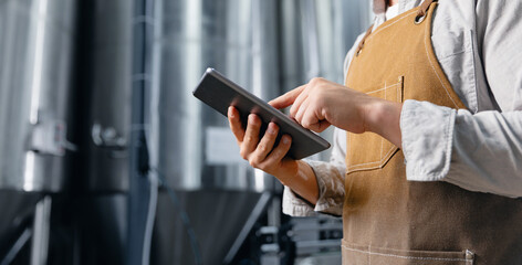 Concept digitalization of food industry with introduction of AI assistants, brewer using tablet in modern brewery with stainless steel tanks