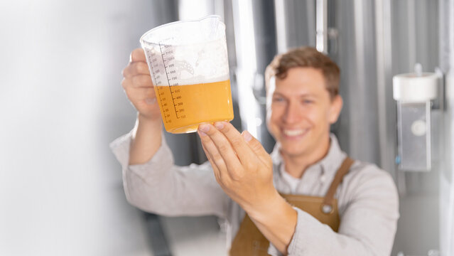 Young caucasian male brewer examining craft light beer sample at brewery. Concept drink industry with quality product banner - Powered by Adobe