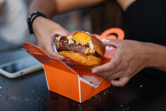 Woman&rsquo;s hands holding a bitten burger