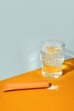 Glass of water and sachet with powder supplements on orange backdrop.