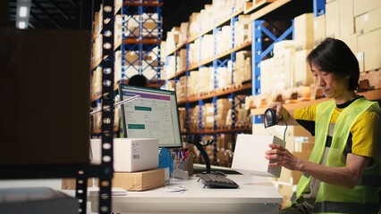 Asian depot worker in hi vis vest scanning barcode labels on boxes, retail operations in industrial fulfillment center. Male staff engages in AWB registration activity for delivery. Camera A.