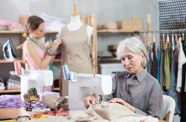 Mature woman is carefully working at a sewing machine and checking the stitches on the fabric...