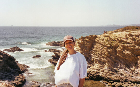 portrait of woman in baseball cap on cliffside beach in Portugal