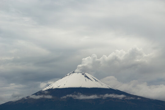 Snow-capped Volcano Emits Smoke Under Cloudy Sky in Daylight