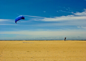 A person kitesurfing on a beach with a blue kite.
