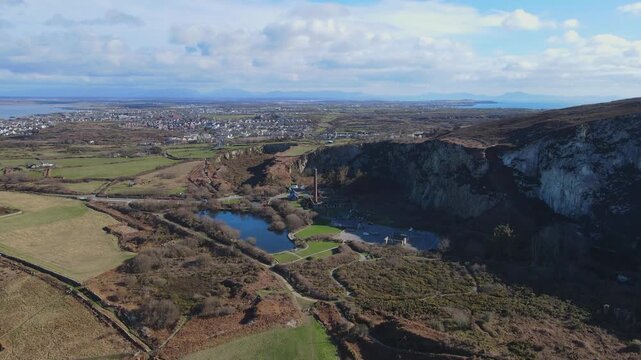 Drone moves past an old mill and car park by a lake towards a large dock town, cruise ship and jetty in background, Holyhead, Anglesey, Wales, 4K, 60fps