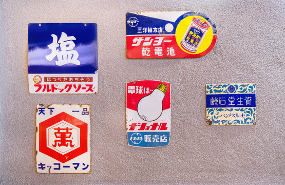osaka, umeda - dec 05 2024: Vintage Japanese rusted advertising enamel signs for Salt, Soy Sauce, dry cell batteries, light bulb and soap showcasing a retro fonts and logos from Showa era on a wall.