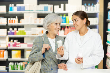 In cosmetic department of pharmacy, young female specialist makes consultation about new serum from manufacturer of beauty care products for mature woman.