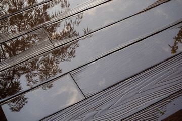 Wet plastic composite decking with puddle reflection after rain. Wood grain composite decking, a beautiful and durable waterproof outdoor flooring solution. Real photo.