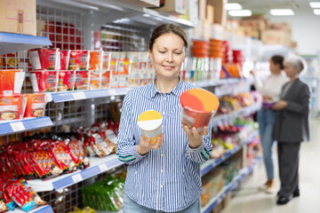 In store near window, woman customer examines package of instant soup in bowl. Female client chooses ready-made food, semi-finished products, for meals on way