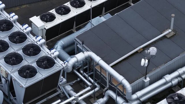 Close-up aerial view of an industrial rooftop in Vilnius, Lithuania, showing large cooling fans, ventilation ducts, and connected piping as part of an HVAC system.