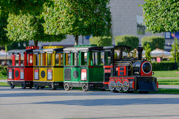 Colorful mini tourist train with red, yellow, and green carriages in a city park on a sunny summer day, outdoor attraction for children and families leisure transport for entertainment and sightseeing