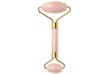 Pink face roller massager with gold accents on transparent background