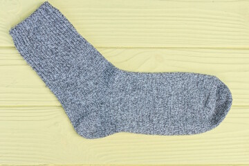 one gray wool long fabric sock lies on a yellow wooden table