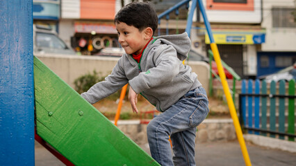Fototapeta premium A boy climbing a green and blue slide at a colorful playground. The image captures the energy and happiness of childhood and outdoor play.