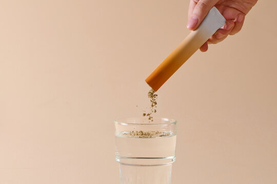 powder being dissolved into a glass of water on an orange background