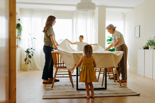 Family putting tablecloth on dining table at home