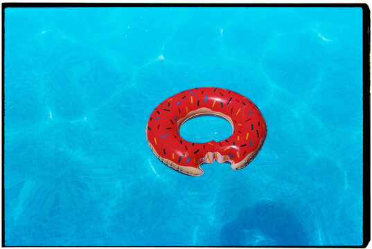 inflatable shaped like a bitten donut in a swimming pool, 35mm