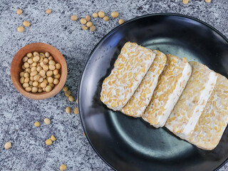 Top view Sliced of Tempeh or tempe on black plate and soy beans on wooden bowl. Tempeh is a traditional Indonesian food made from fermented soy beans. Isolated on white background.