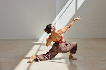 Dancer performing an expressive movement in a sunlit studio