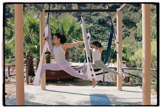 Two Women Practicing Aerial Yoga Outdoors Near Tropical Palm Trees - Powered by Adobe