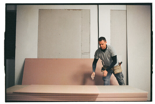 Worker taking sheet of drywall at construction site