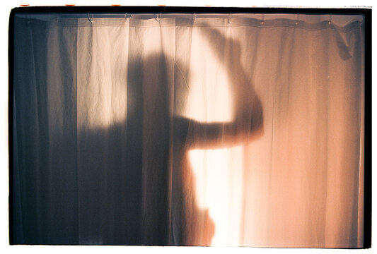 Man taking shower behind translucent curtain