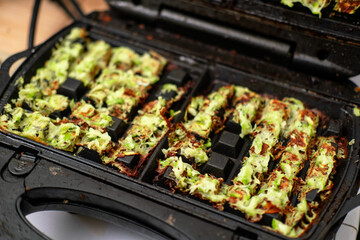 Zucchini waffles cooking in waffle maker with crispy texture and golden brown color.