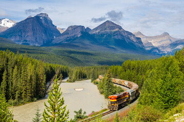 Freight train curving through dense forest with towering mountains in Banff