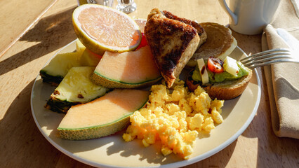 Colorful breakfast plate featuring fresh fruits, scrambled eggs, and toast, beautifully arranged on a wooden table, showcasing a vibrant morning meal