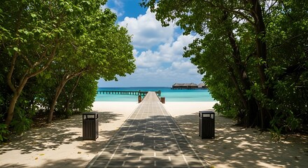 A paved pathway leads through lush green trees to a sandy beach and a wooden pier stretching into the turquoise ocean